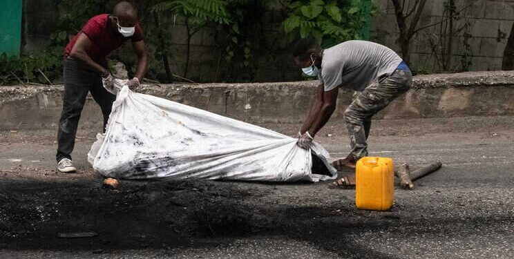 epa10605579 Two men cover the cremated body of a person in Port-au-Prince, Haiti, 02 May 2023. At least five people were killed on 02 May 2023 by the population in Petion-ville, Port-au-Prince, for being alleged members of the Ti Makak armed group, dismantled a few weeks ago by the National Police.  EPA/Johnson Sabin