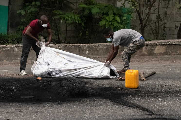 epa10605579 Two men cover the cremated body of a person in Port-au-Prince, Haiti, 02 May 2023. At least five people were killed on 02 May 2023 by the population in Petion-ville, Port-au-Prince, for being alleged members of the Ti Makak armed group, dismantled a few weeks ago by the National Police. EPA/Johnson Sabin